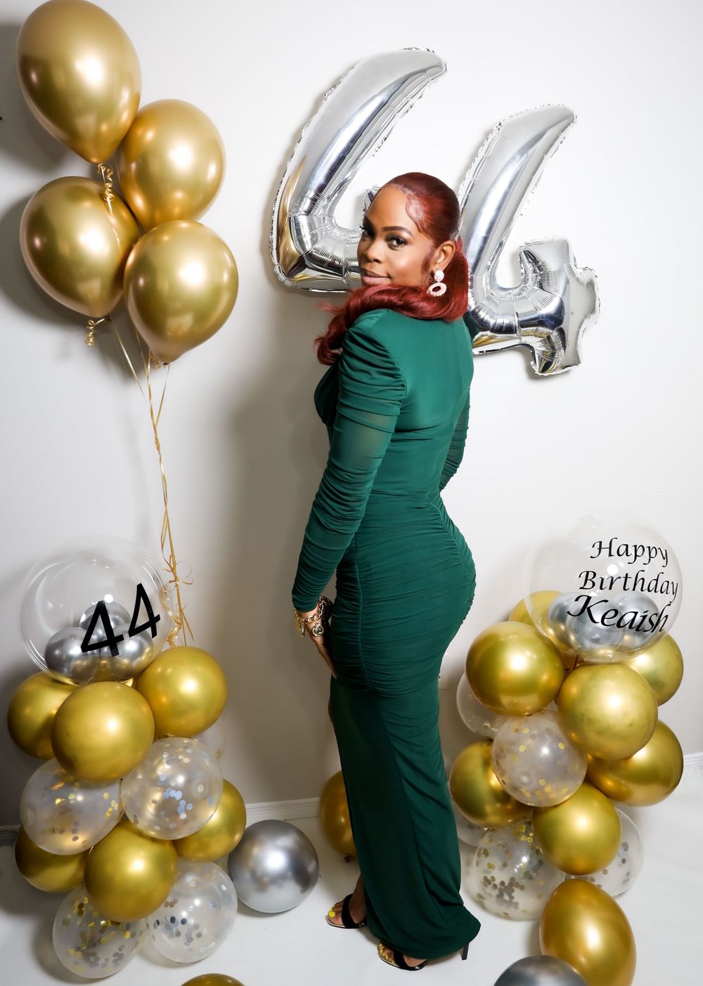 44th birthday photo with green dress and gold balloon decorations against white background.
