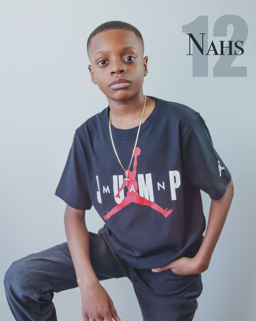 Young person wearing a dark Air Jordan t-shirt and necklace poses against a grey background.