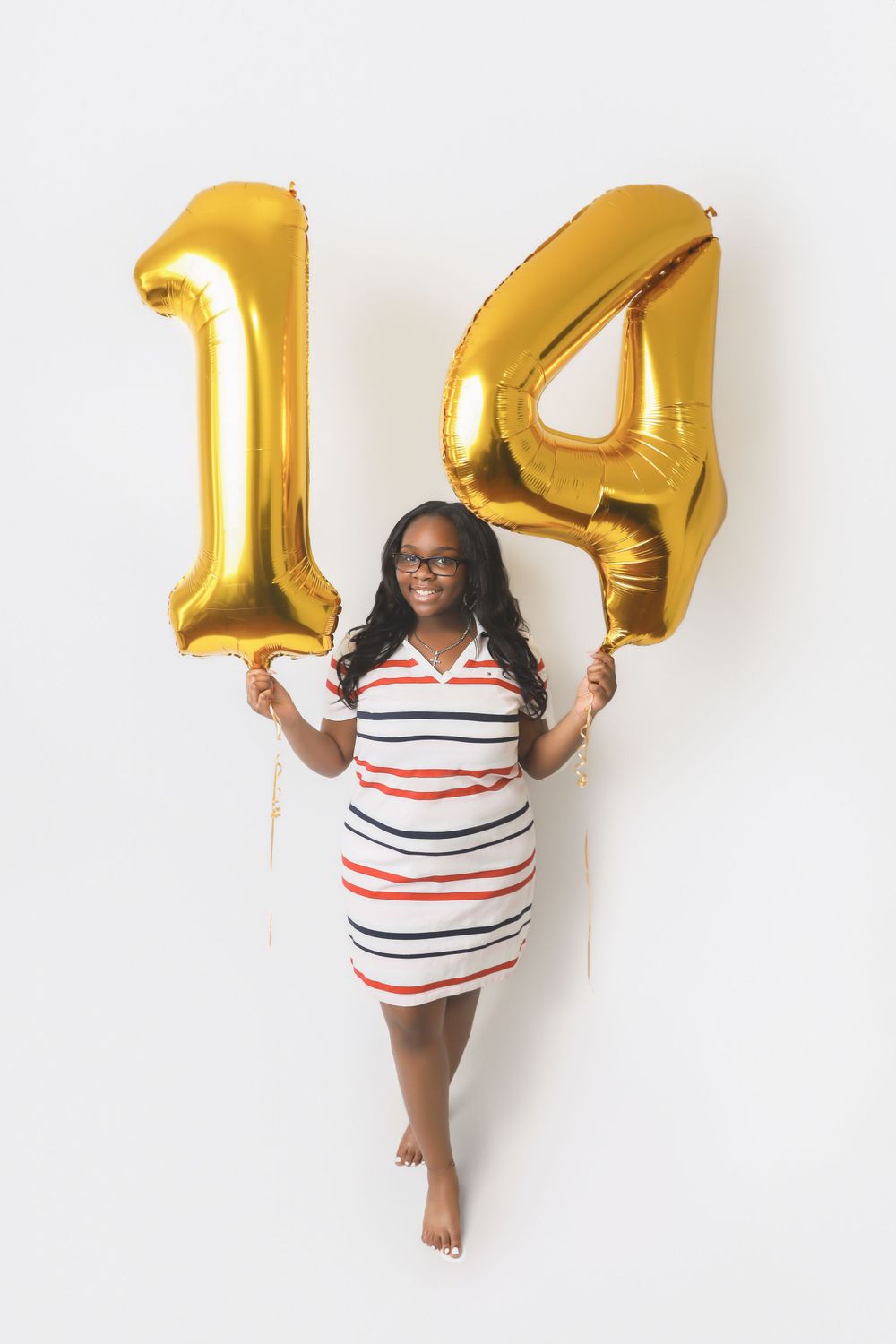Celebratory photo with large gold number 14 balloons and striped dress against white background.