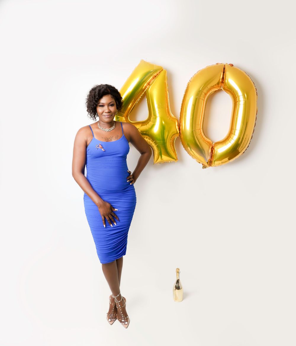 Birthday celebration photo with blue dress and gold number 40 balloons against white wall.
