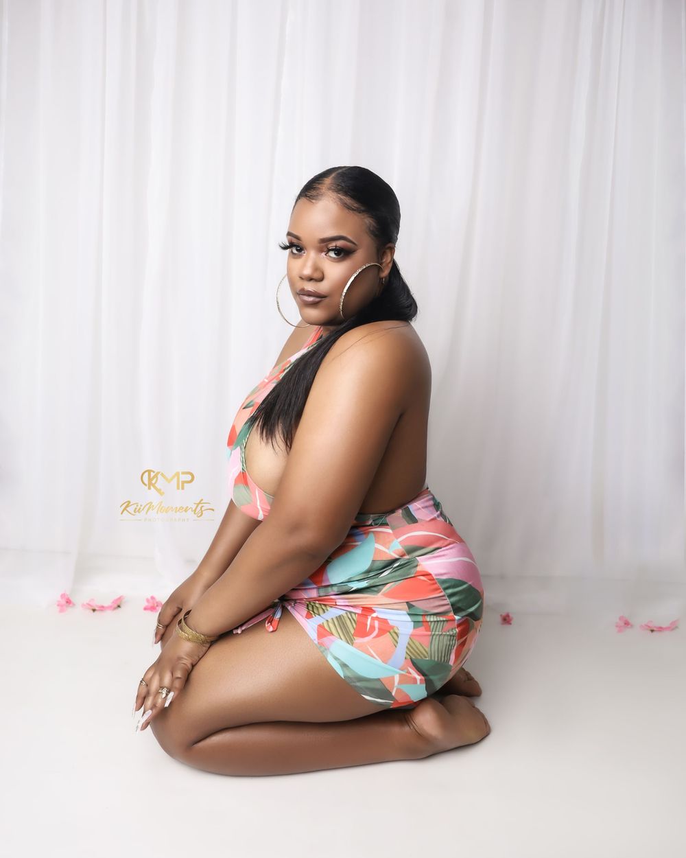 Portrait in floral print outfit against white curtain backdrop with pink decor elements.