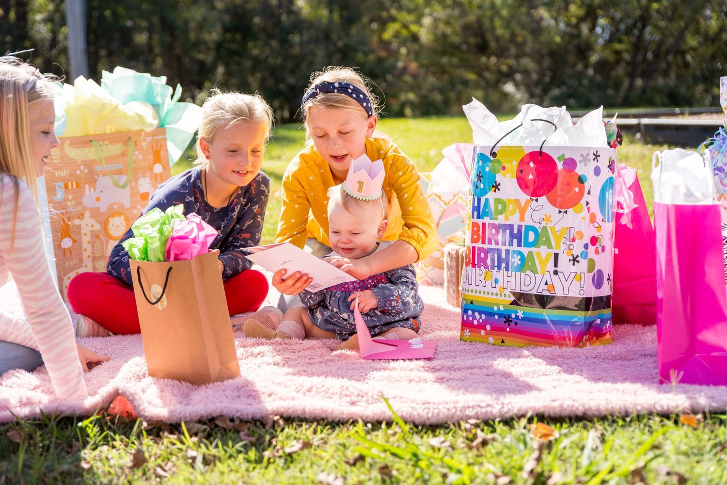 An older sister reading a birthday card to her baby sister surrounded by gifts