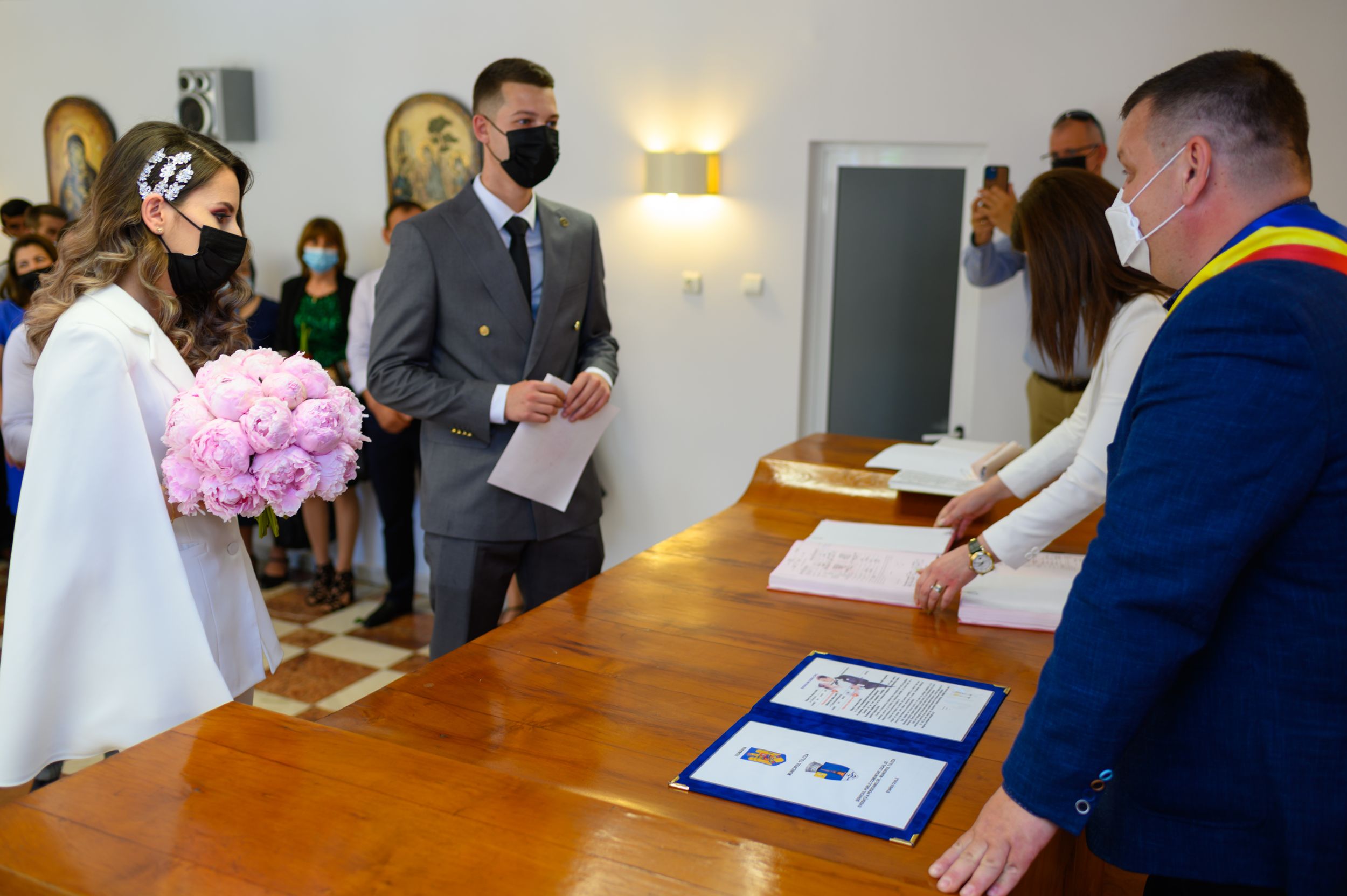 A couple signing marriage documents at a wooden desk during a civil ceremony.