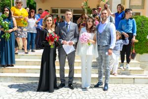 A group photo of wedding attendees gathered on stone steps outside a building.