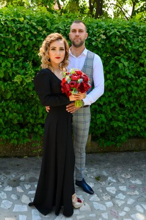 Romantic portrait of couple in black dress and plaid vest holding red roses.
