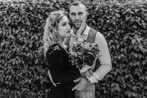 Black and white portrait of couple embracing against ivy wall.
