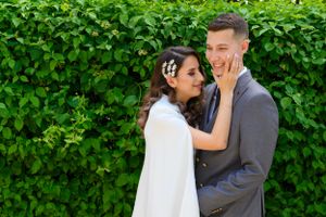 Romantic couple shares an intimate moment against a lush green hedge backdrop.
