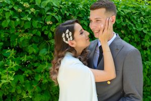 Couple embraces tenderly in front of vibrant green foliage.