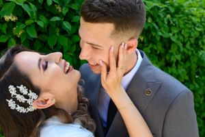 Couple in wedding attire share a tender moment against greenery.