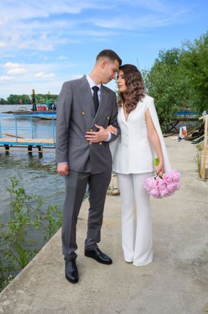 Wedding couple poses on waterfront path with lake and blue sky in background.