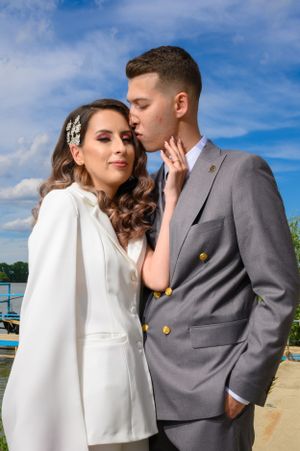 Couple in wedding attire shares intimate moment by lakeside on sunny day.