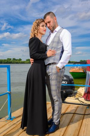 Couple in formal attire embracing on wooden dock during daytime photo session.