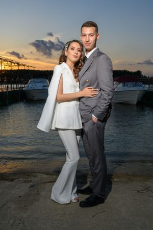 Couple in matching light outfits posing for photos at waterfront during sunset.