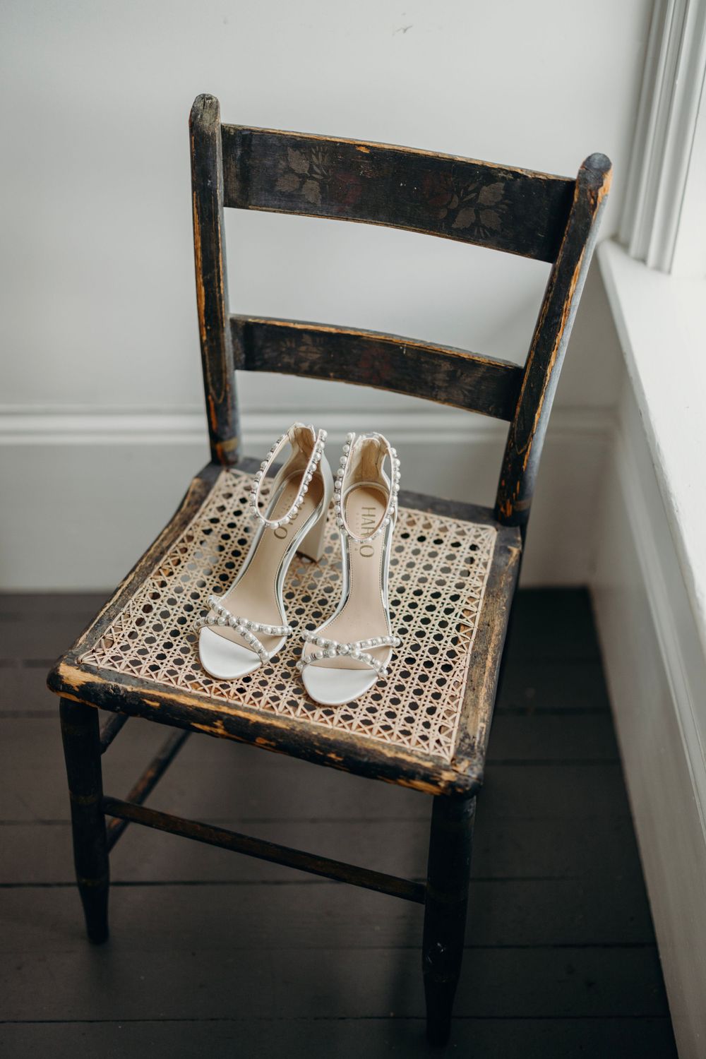 White bridal shoes placed on a vintage dark wood chair with cane seat.