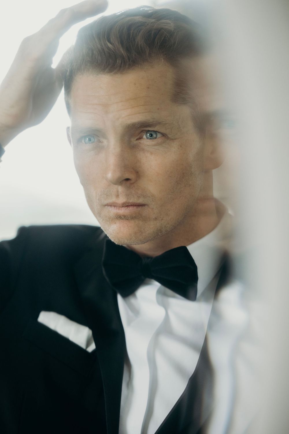 Artistic portrait through frosted glass showing formal attire and bow tie.