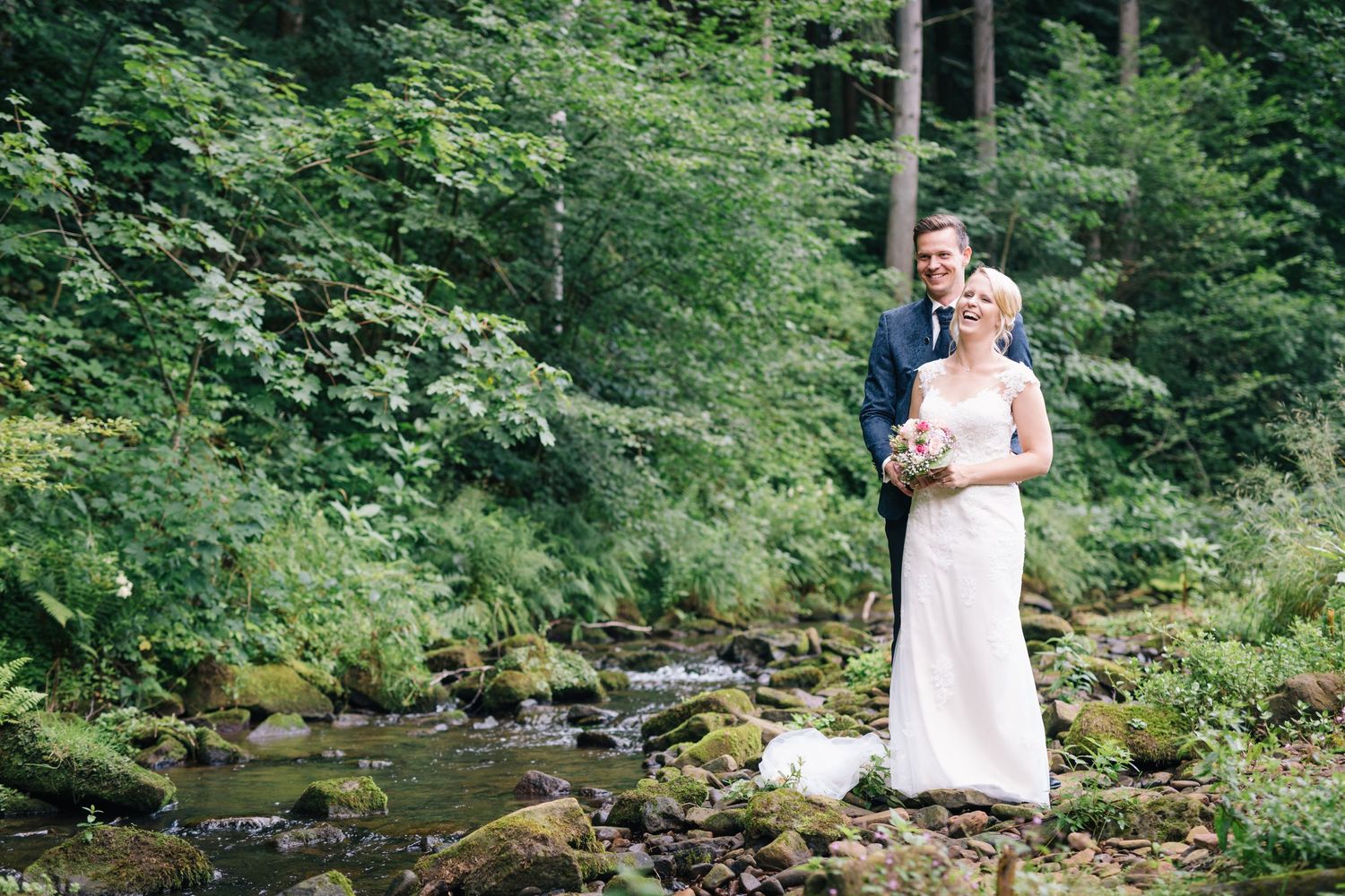 Hochzeitsfotografie - Brautpaar steht am Bach im Wald