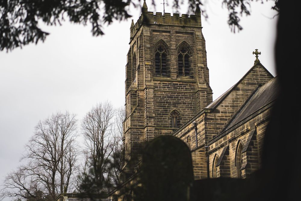 A gothic stone church tower photographed through tree branches against an overcast sky.