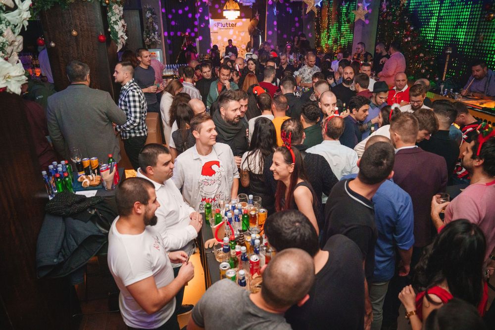 Crowded bar scene with patrons gathered around tables filled with colorful drinks.