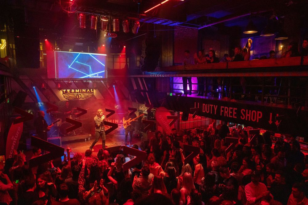 Packed nightclub venue with red lighting and projected logo during live performance.