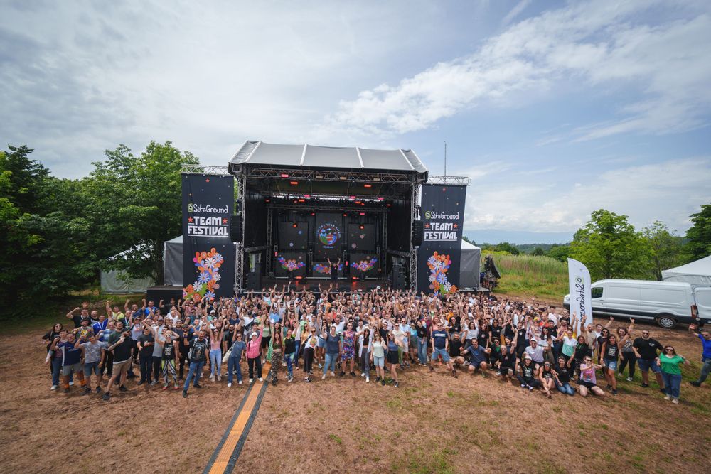 Large outdoor festival crowd gathered in front of a concert stage under blue sky.