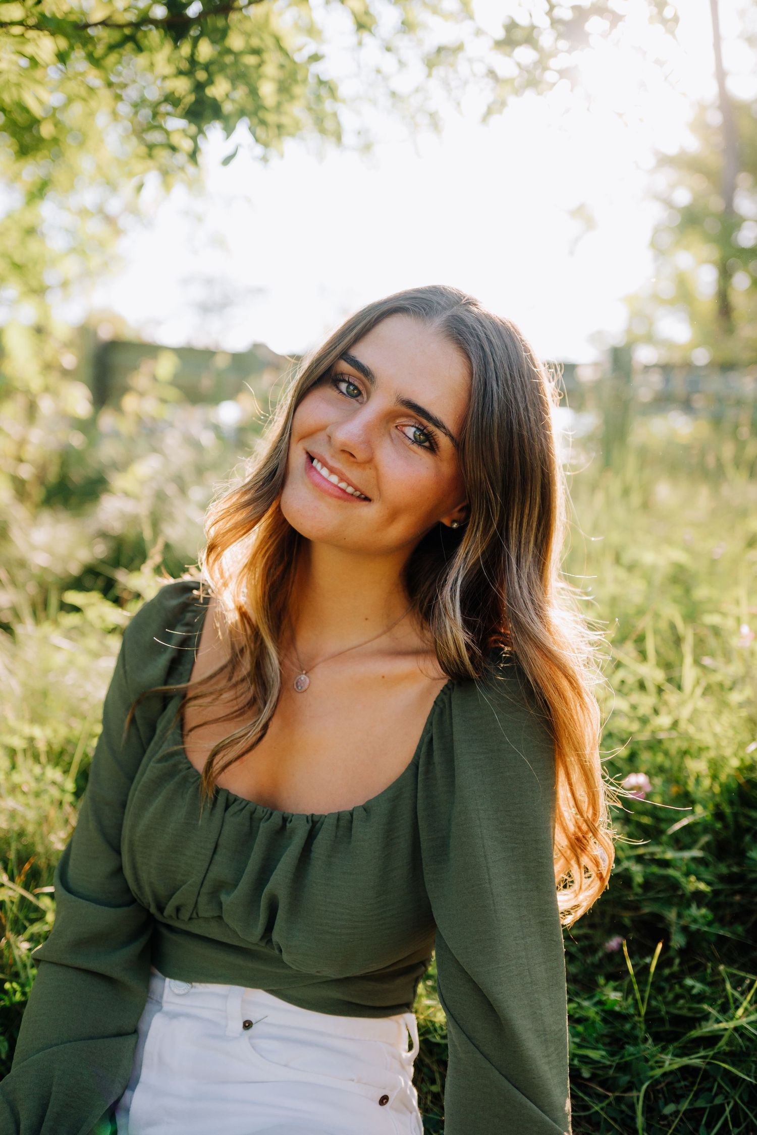 Natural outdoor portrait of someone in a green top and white pants with sunlit background.