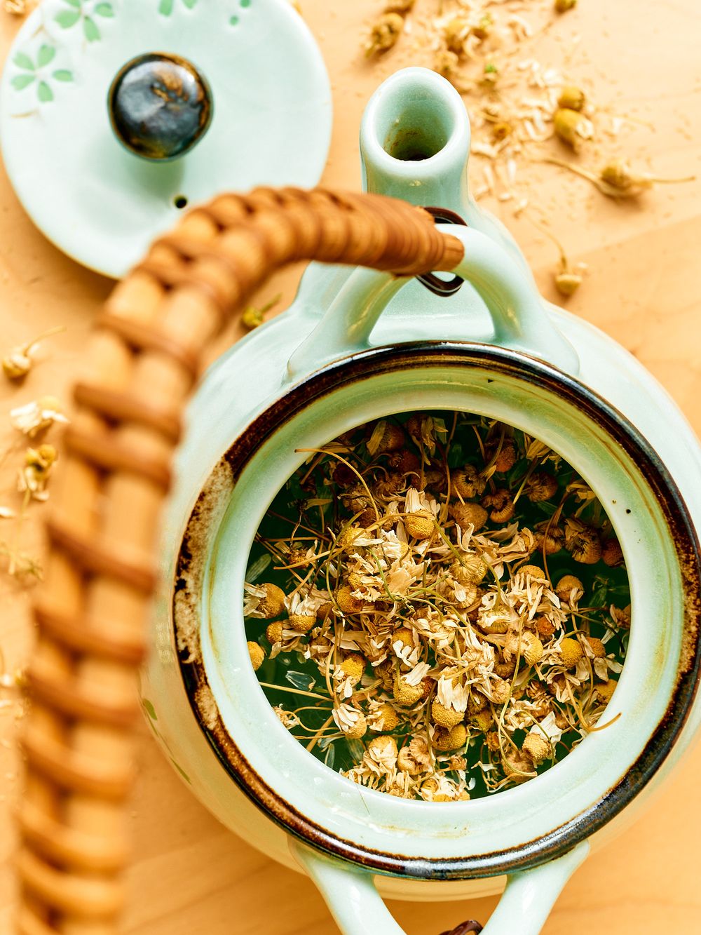Top view of loose chamomile tea leaves inside a mint green teapot with bamboo handle.