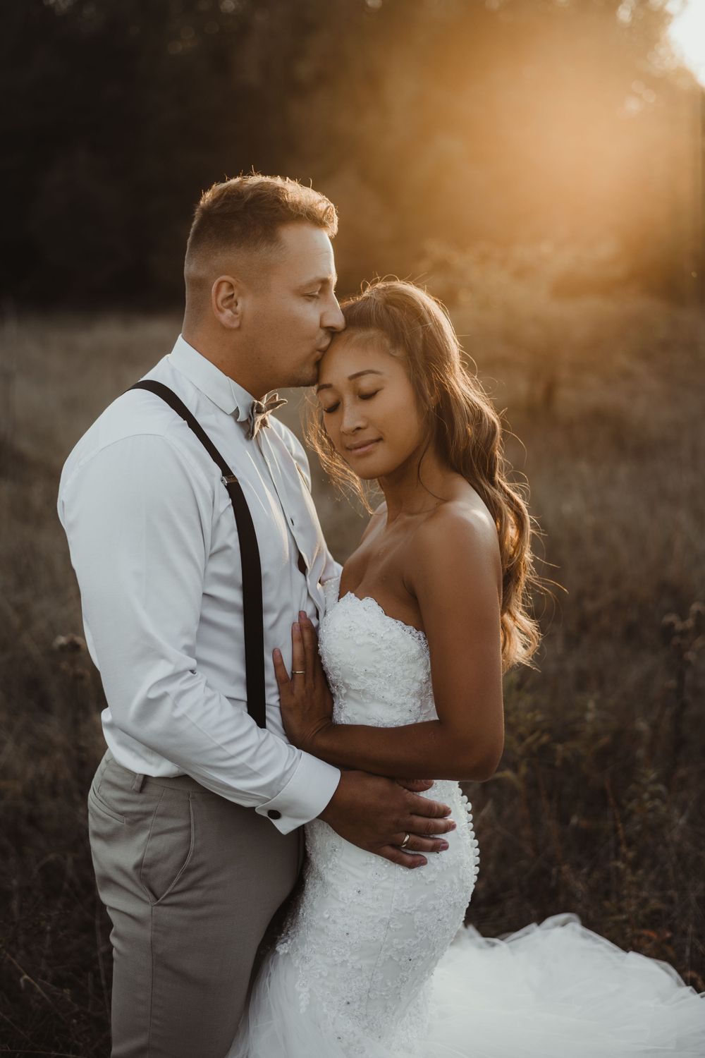 Romantic sunset portrait of newlyweds embracing in golden field during golden hour.
