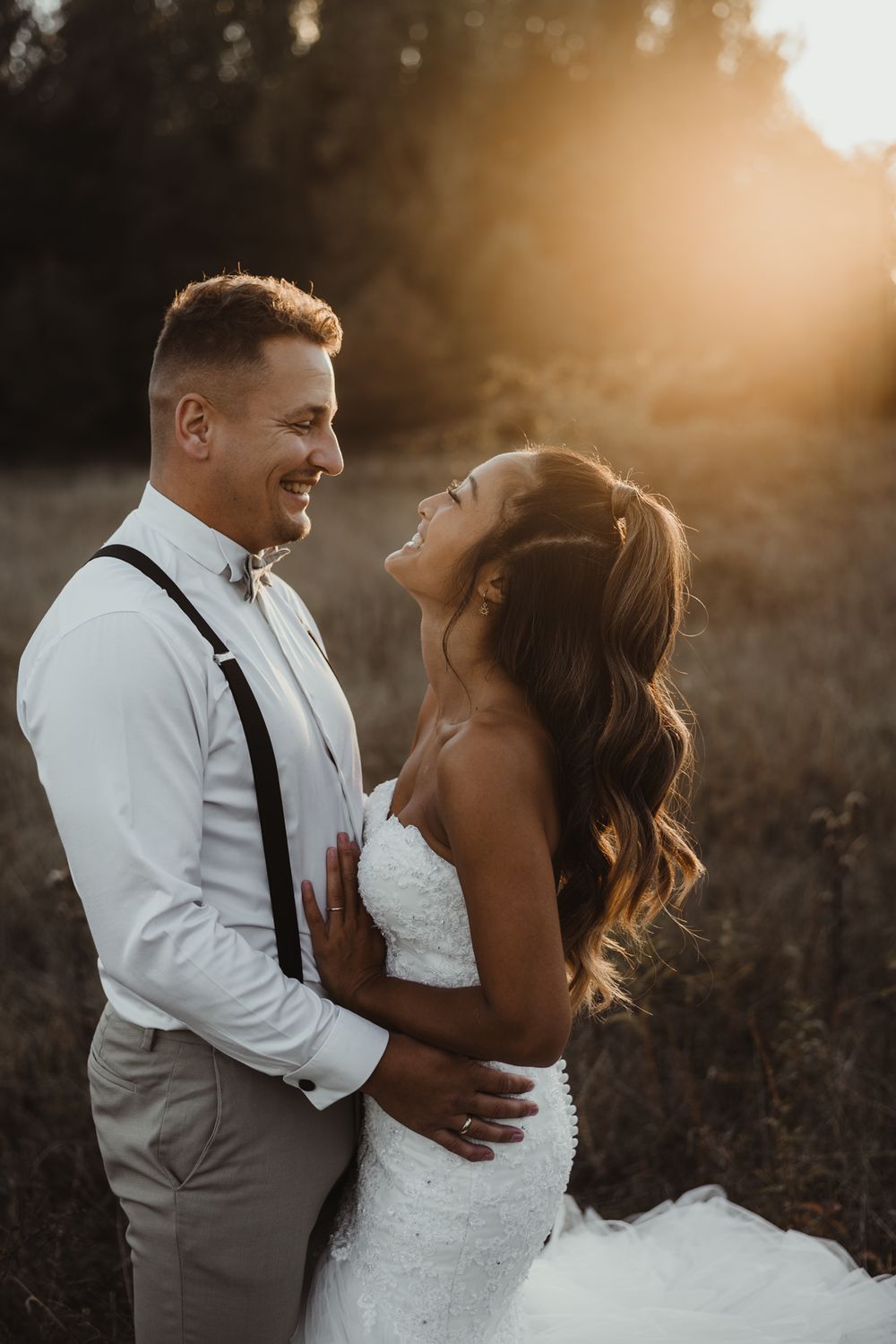 A candid wedding photo captures a couple sharing a loving laugh in golden hour light.