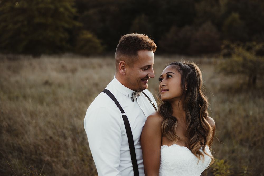 A close-up wedding portrait shows an intimate moment between newlyweds in a rustic outdoor setting.