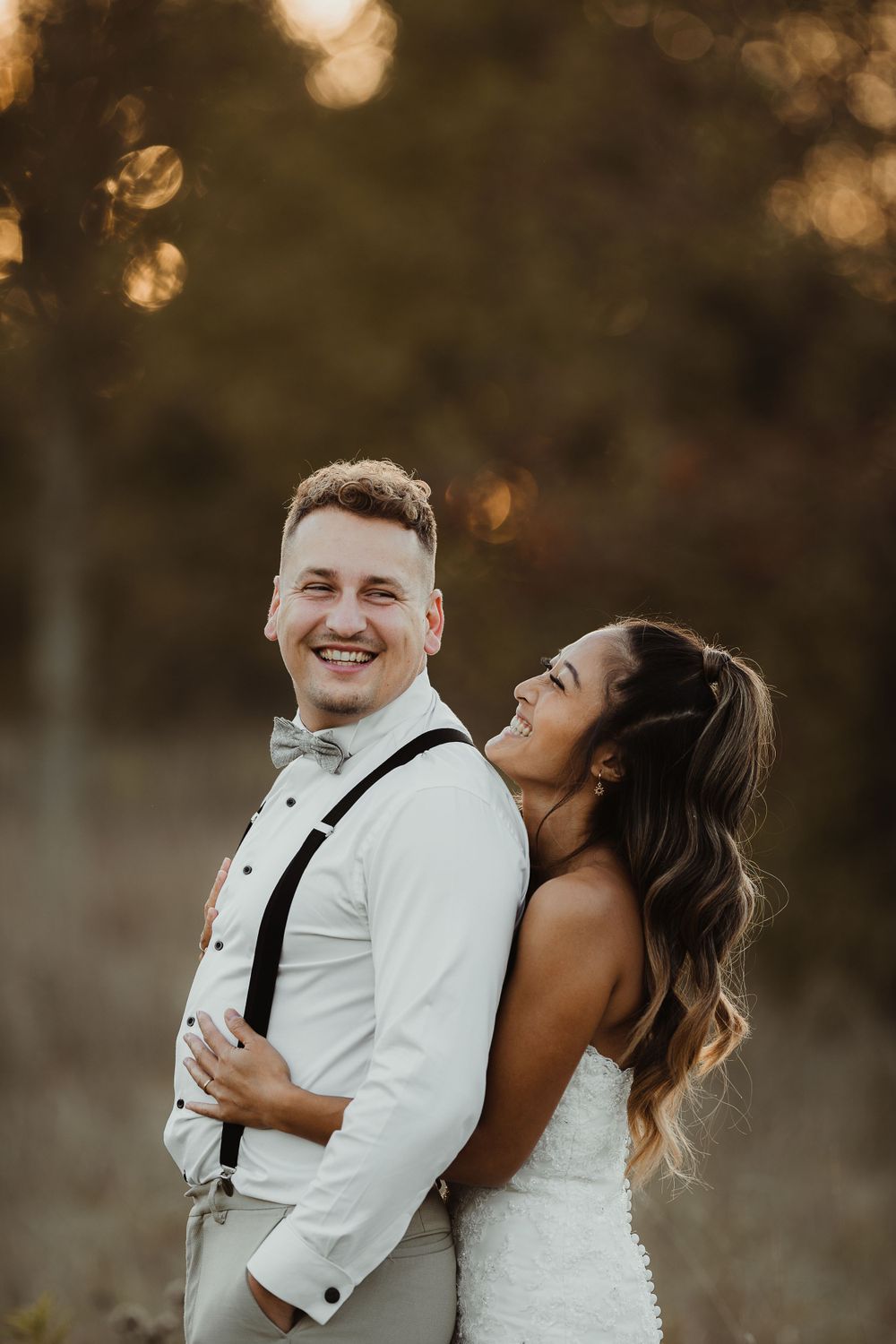 Joyful wedding couple laughing together in warm evening light with natural bokeh background.