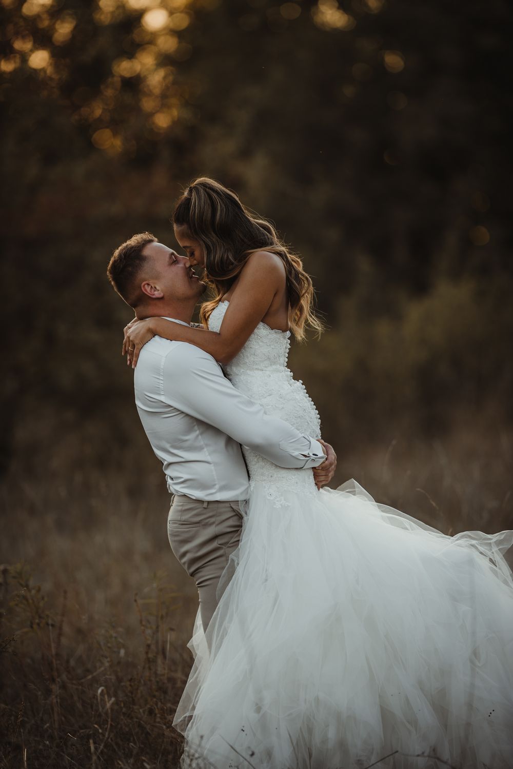 A groom lifts his bride in a romantic embrace during their sunset wedding photoshoot.