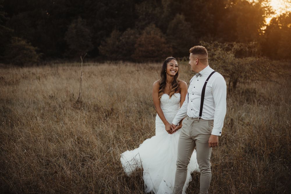 A romantic wedding photo captured in a golden field at sunset with muted earth tones.