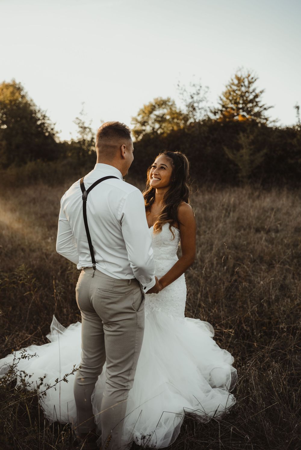 A joyful wedding couple shares a laugh in a golden field during their sunset photoshoot.