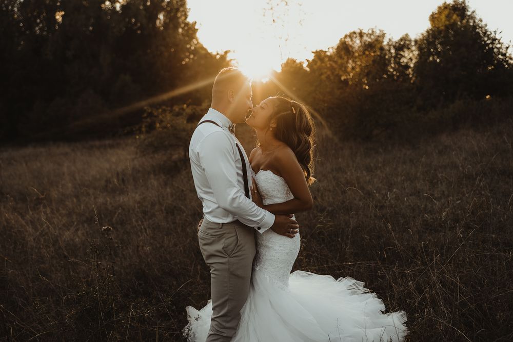 Intimate wedding portrait silhouetted against a dramatic sunset in a rustic field setting.