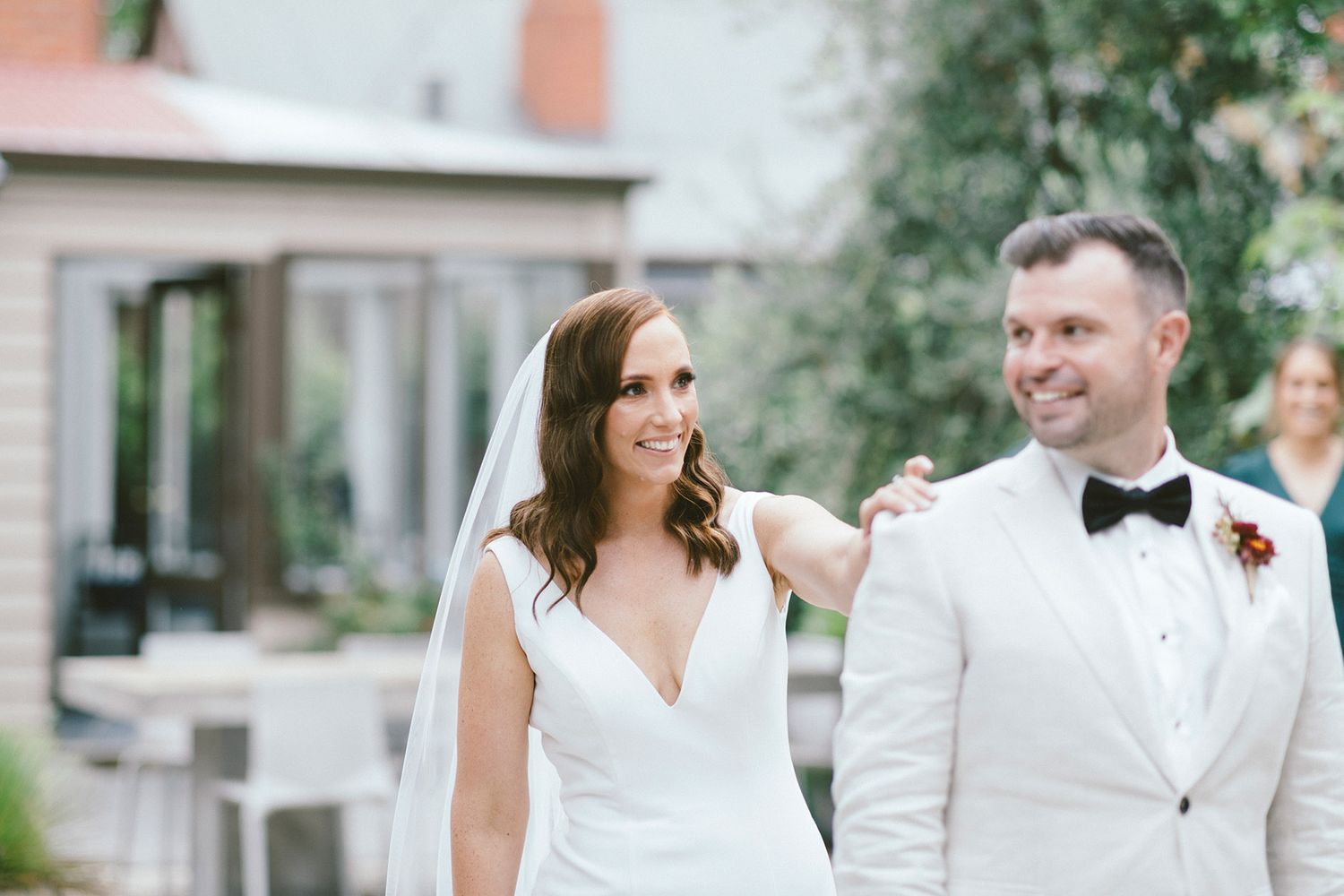 A couple in wedding attire share a joyful moment in an outdoor garden setting.