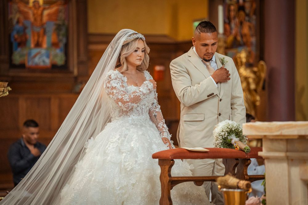Bride in lace ball gown with veil and groom in beige suit stand at church altar.