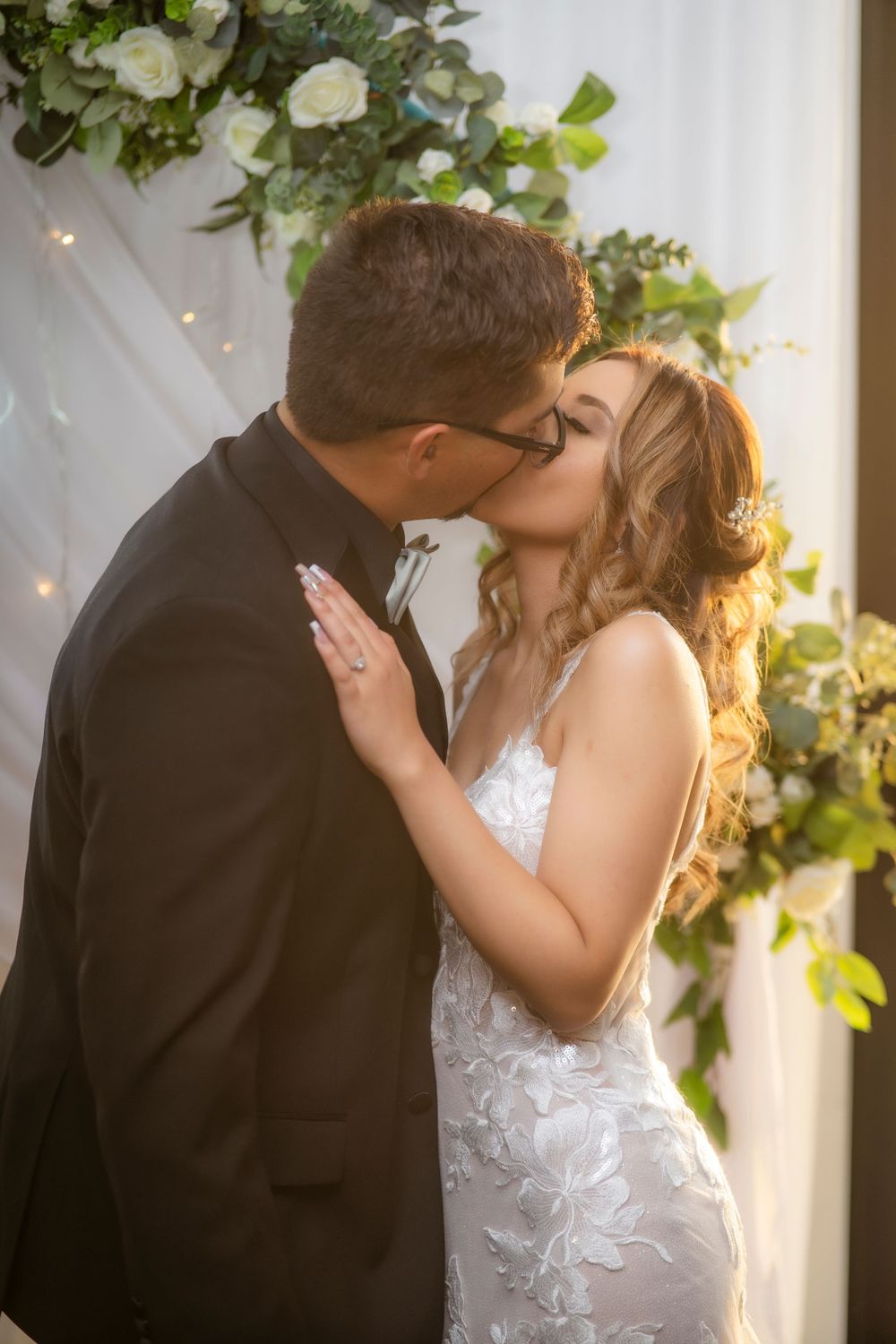 Bride and groom sharing their first kiss at a floral wedding altar with white roses and greenery.