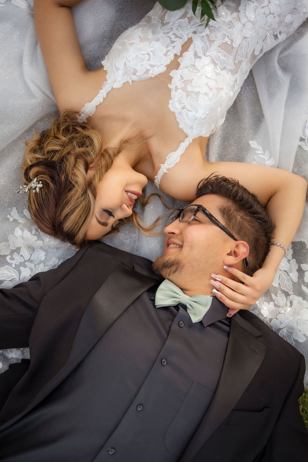 Bride and groom lying down smiling at each other, groom in black tuxedo with mint bow tie.