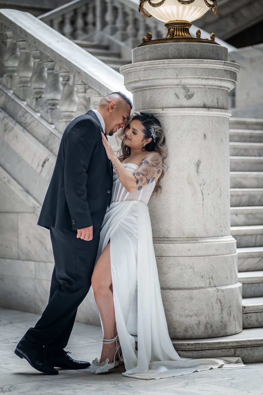 Elegant wedding couple shares intimate moment by marble column and grand staircase.