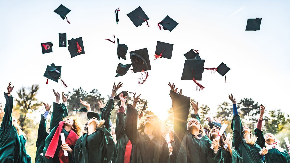 Graduates throw mortarboards into air during sunset celebration ceremony.