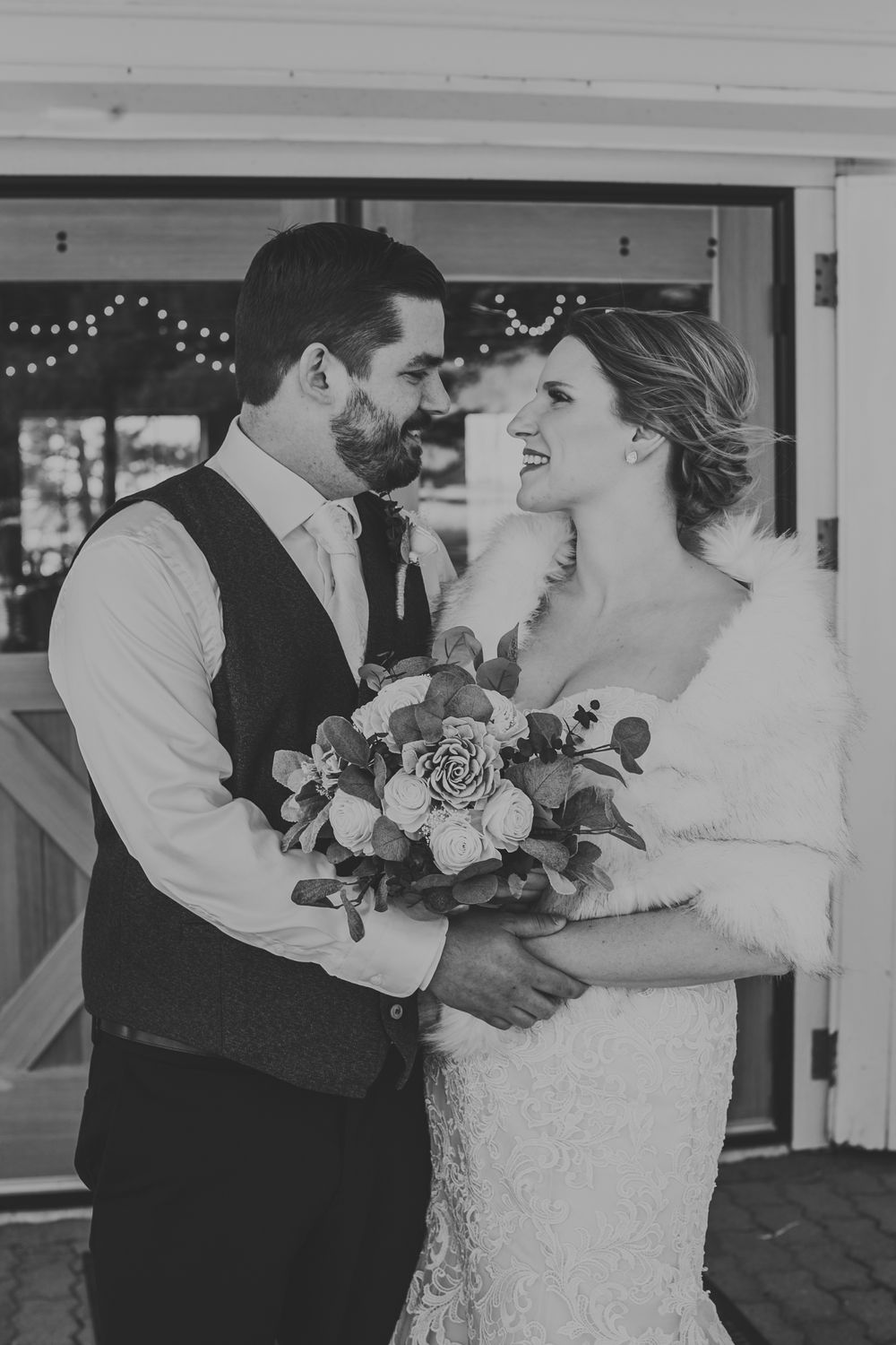 Black and white photo of bride and groom sharing a tender moment, bride holding a floral bouquet at winter wedding.