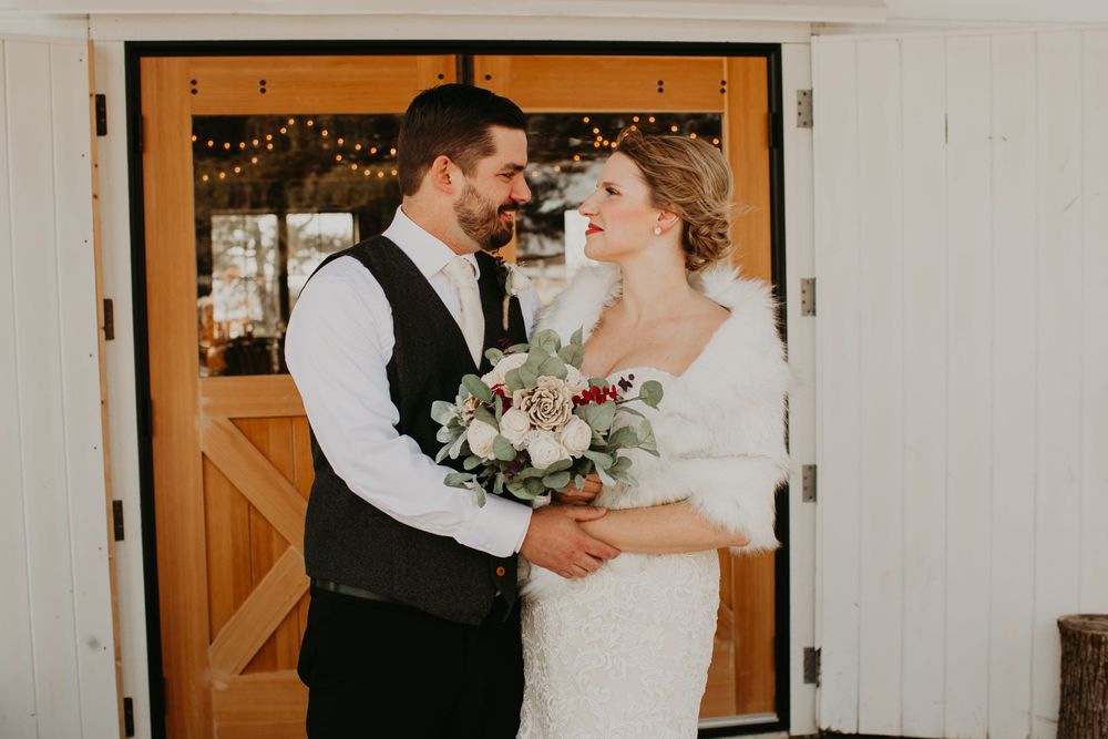 Bride and groom gazing at each other lovingly in front of rustic barn doors adorned with string lights.