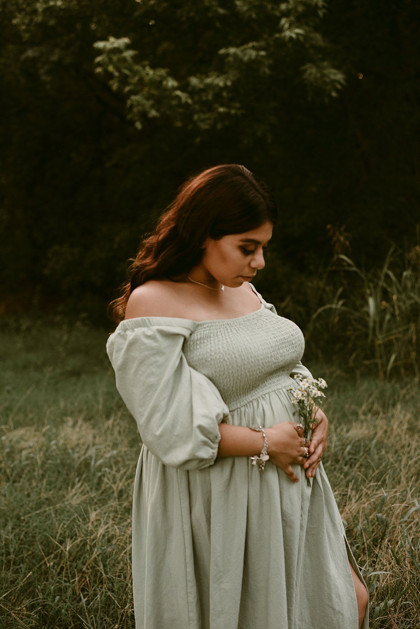 A dreamy outdoor portrait features someone in a flowing off-shoulder dress holding wildflowers at sunset.