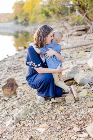 Intimate waterside portrait of parent and child in navy blue dress on rocky shore in Springfield, MO.