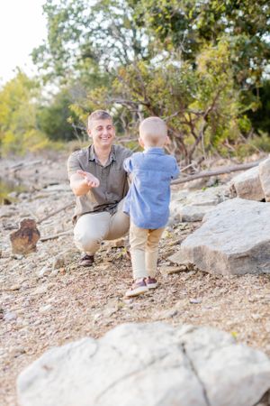 Parent and toddler share a playful moment on rocky terrain near water in Springfield, MO.