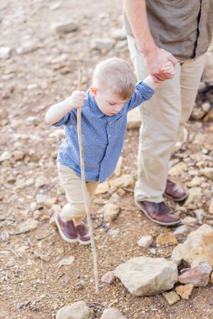 Toddler in blue sweater explores rocky terrain while holding parent's hand in Springfield, MO.