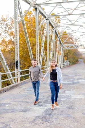 Couple walking together on a metal bridge during autumn with fall colors in background in Springfield, MO.