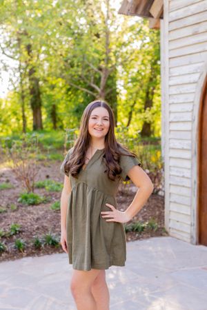 Young woman in olive green dress poses in front of white chapel wall in Springfield, MO.