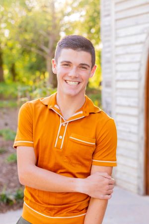 Young person in bright orange polo shirt smiling outdoors on sunny day with greenery in background in Springfield, MO.