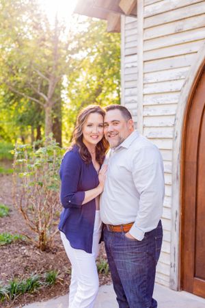 Couple in casual attire poses together against white wooden wall on sunny day in Springfield, MO.